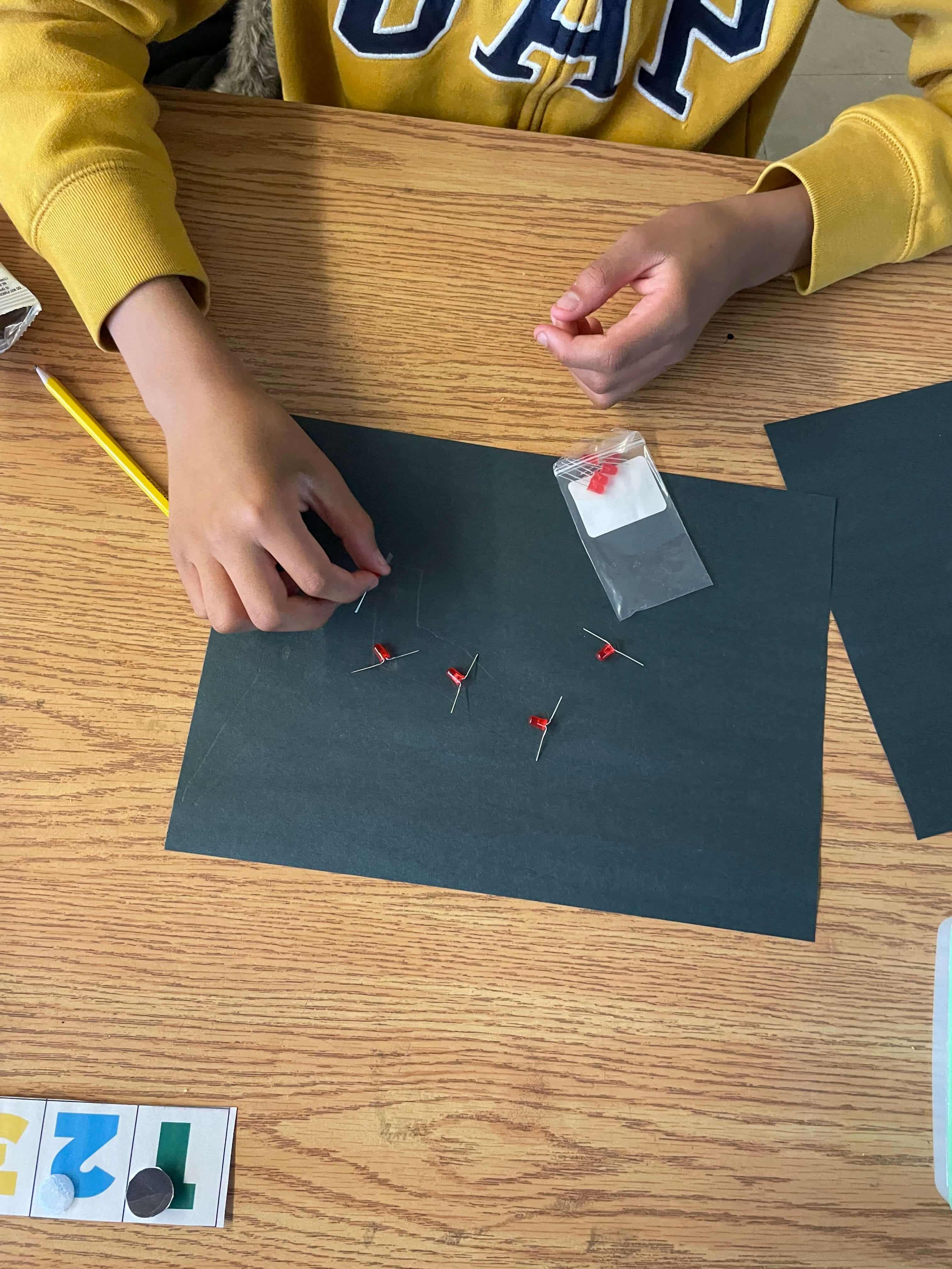 A student in a yellow sweater placing red LEDs onto a piece of black construction paper.